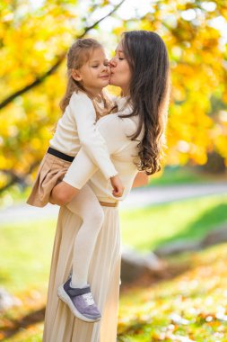 Anne ve kızı sonbahar parkında birlikte güzel vakit geçiriyorlar. Etrafı renkli ağaçlar ve yapraklarla çevrili. Neşeli bir bağ ve aşk anı. Yüksek kalite fotoğraf