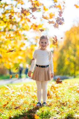 Sonbahar parkında oynayan ve eğlenen küçük bir kız. Etrafı renkli yapraklarla çevrili. Sonbahar sezonu boyunca doğada neşeli, kaygısız bir çocukluk anı. Yüksek kalite fotoğraf
