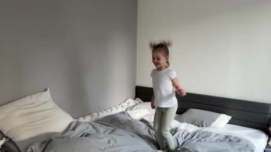 Evdeki yatak odasında ailesinin yatağına atlayan küçük bir kız. Çocukluğunda neşeli enerji, neşe ve hareket özgürlüğü kavramı. Yüksek kalite 4k görüntü