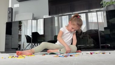 Küçük kız yerde oturuyor ve oturma odasındaki yapı taşlarıyla oynuyor. Erken gelişim kavramı, yaratıcılık ve ev ortamında odaklanmış oyun. Yüksek kalite 4k görüntü