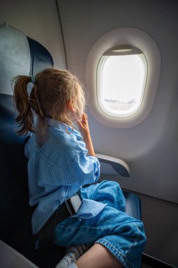 Uçuş sırasında uçağın camından dışarı bakan küçük bir kız. Merak, seyahat deneyimi ve havada çocukluk merakı. Yüksek kalite fotoğraf