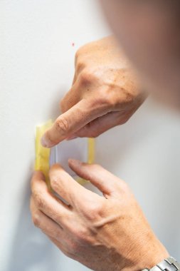 Duvarı beyaza boyamadan önce adam lambanın düğmesini bantla kapatıyor. Ev tadilatı, yüzey koruması ve iç işleri sırasında dikkatli bir hazırlık. Yüksek kalite fotoğraf