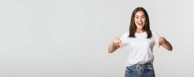 Tatmin olmuş, gülümseyen esmer kız parmaklarını aşağı uzatıyor, ürün öneriyor..