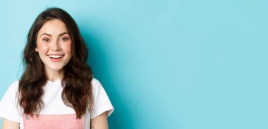 Şaşırmış ve heyecanlı gülümseyen kızın ilginç teklifini kontrol eden, ilgi çekici kameralara bakan, mavi arka planda duran.