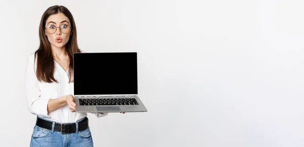 stock image Portrait of cute girl in glasses, student showing laptop screen with amazed face, standing over white background. Copy space