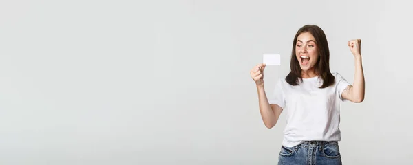 stock image Joyful good-looking girl rejoicing and looking at credit card, fist pump while triumphing, white background.