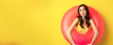Pembe yüzme ringinin içindeki seksi kadının portresi, plaj tatili, tatil ve yaz konsepti, sarı arka plan..