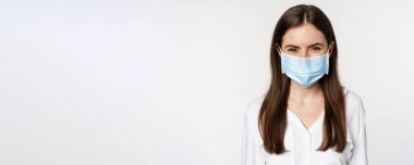Covid-19 and pandemic concept. Young office woman wearing medical mask during coronavirus social distancing, standing over white background.