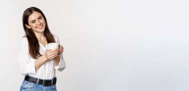 Corporate woman standing with coffee tea mug and smiling, drinking from cup, standing happy against white background.