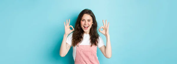 Stock image Very well, alright. Excited smiling brunette guy say yes, showing okay signs and agree with you, praising good job, standing happy against blue background.