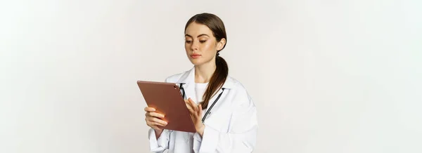 stock image Doctor in white coat using digital tablet, reading medical data on gadget, working in hospital, standing over white background.