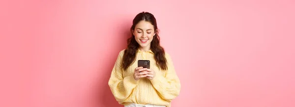 年轻的黑发女人的画像 阅读智能手机屏幕和微笑 在社交媒体应用程序上聊天 在网上购物 站在粉色背景下 — 图库照片