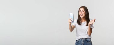 Arkadaşça gülümseyen bir kadın videosu. Akıllı telefondan arıyor ve konuşuyor. Mutlu, beyaz arka planda duruyor..