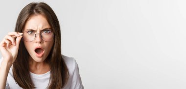 Hakarete uğramış ve şok olmuş genç ve kızgın bir kadın gözlüklerinin altından bakıyor..