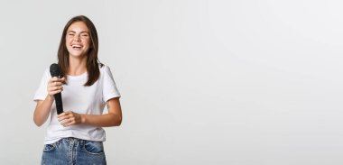 Mutlu gülen kız mikrofon tutuyor ve karaoke söylüyor, beyaz arka plan.