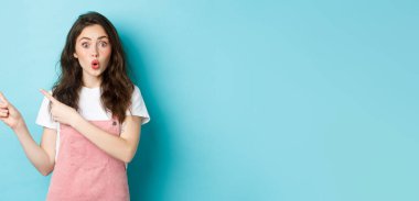 Vay canına, şuna bak. Şaşırmış esmer kadın model dudaklar büzüşüyor ve ilgi çekici görünüyor, parmaklarını ilginç bir şeye doğrultuyor, afiş gösteriyor, mavi arka plan..