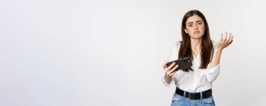Mobil video oyununda kaybeden üzgün kadın, akıllı telefondan üzgün ve hayal kırıklığına uğramış görünüyor, somurtuyor, beyaz arka planda duruyor..