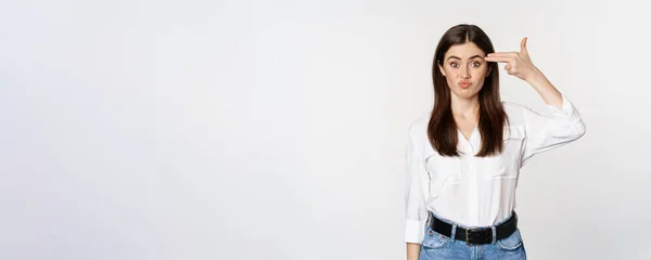 stock image Image of annoyed young woman showing finger gun gesture over head, bothered by smth, tired, standing over white background.