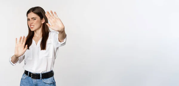 stock image Displeased woman showing stop, rejection gesture, waving hands to decline, refuse of something ugly, standing over white background.