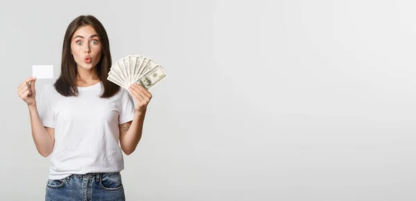 有名なブルネットの女の子は興奮している お金とクレジットカードを保持し 白い背景に立って — ストック写真