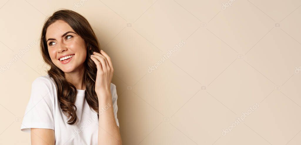 Close up portrait of coquettish beautiful girl gazing silly, gently smiling and giggling, posing flirty and cute against beige background. Women beauty and valentines concept.