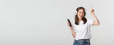 Güzel esmer kız dans ediyor ve kablosuz kulaklıkla müzik dinliyor, elinde akıllı telefon tutuyor..