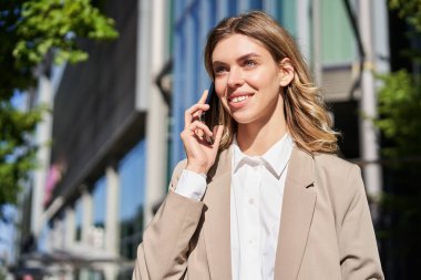 İş kadını portresi telefon görüşmesi yapıyor, ofis binasının yanındaki caddede duruyor, telefonda biriyle konuşuyor..