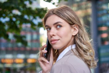 İş kadınının cep telefonuyla konuşmasını yakından çek. Şirket kadını birini arıyor, etrafa bakıyor, dışarıda duruyor..