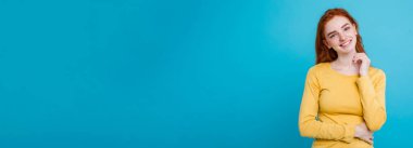 Kameraya bakarak gülen çiller ile mutlu Kızıl kızıl saçlı kız portresi. Pastel mavi arka plan. Kopya alanı.