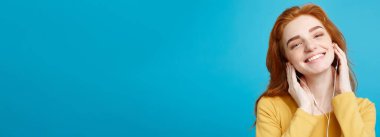 Yaşam tarzı kavramı - neşeli mutlu Kızıl kızıl saçlı kız portresi zevk kameraya gülümseyen neşeli kulaklık ile müzik dinlemek. Pastel mavi arka plan üzerinde izole. Kopya alanı