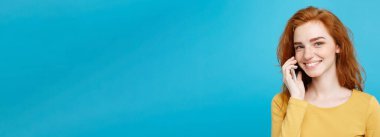 Yaşam tarzı ve teknoloji kavramı - eğlenceli ve heyecan verici arkadaşla cep telefonuyla konuşurken ile neşeli mutlu Kızıl kızıl saçlı kız portresi. Pastel mavi arka plan üzerinde izole. Kopya alanı