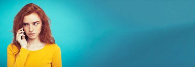 Yaşam tarzı kavramı - Kızıl kızıl saçlı kız arkadaşı ile cep telefonuyla konuşurken şok edici ve stresli ifade ile portresi. Pastel mavi arka plan üzerinde izole. Kopya alanı.