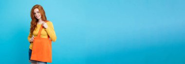 Alışveriş kavramı - turuncu alışveriş çantası ile gülümseyen portre genç güzel çekici Dişileştirilmiş kız yakından. Mavi Pastel renkli