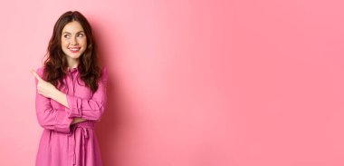 Makyajlı, bahar kıyafeti giyen, logoya bakan, sol telif alanındaki afişi gösteren, pembe arka planda duran çekici bir kız..