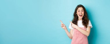 Koyu renk bukleli mutlu bir kadının portresi, büyülenmiş bir gülümseme, logo afişini gösteren parmaklar, mavi arka planda duran bir reklamı gösteriyor..