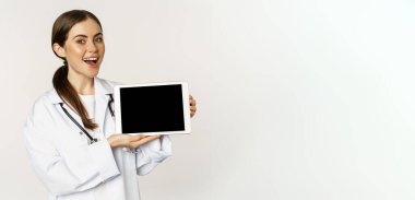 Çevrimiçi tıbbi yardım, uzaktan randevu. Gülümseyen güzel kadın doktor dijital tablet ekranı gösteriyor, web sitesi logosunu gösteriyor, beyaz arka planda duruyor..