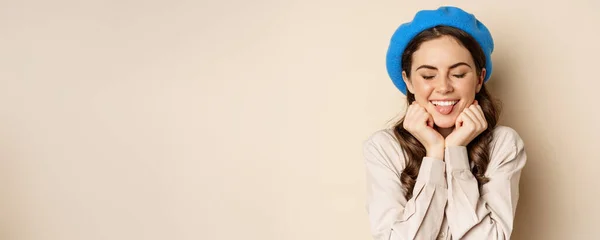 stock image Close up portrait of feminine young woman in trendy french hat, posing cute and romantic, making silly coquettish face and tender smile, beige background.