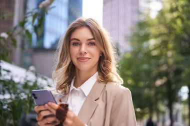Şirket kadınının yakın portresi, genç stajyer caddeden ofise yürüyor, cep telefonunu tutuyor, akıllı telefondan mesajlar atıyor..