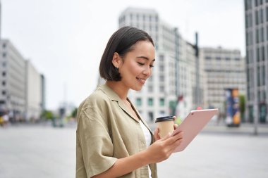 Sokakta yürüyen, tablet okuyan ve dışarıda kahve içen Asyalı kız..