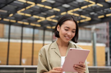 Tablet kullanan, okuyan, sokakta duran güzel Asyalı kızın portresi..