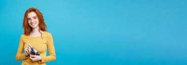 Portre genç güzel çekici zencefil kız mutlu vintage fotoğraf makinesi ile gülümseyen ve seyahat etmeye hazır kapatın. Pastel mavi arka plan üzerinde izole. Kopya alanı