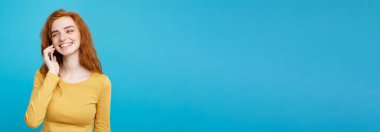 Yaşam tarzı ve teknoloji kavramı - eğlenceli ve heyecan verici arkadaşla cep telefonuyla konuşurken ile neşeli mutlu Kızıl kızıl saçlı kız portresi. Pastel mavi arka plan üzerinde izole. Kopya alanı