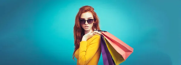 ショッピングのコンセプト ショッピング バッグとカメラを見て笑っている肖像若い美しい魅力的な Redhair 女の子をクローズ アップ 青いパステル背景 コピー スペース — ストック写真