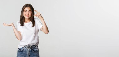 Şüpheci ve eğlendirilmemiş esmer kız çok küçük, minicik bir şey gösteriyor..