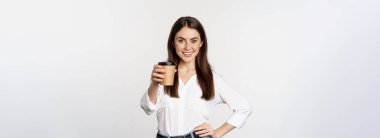 Image of modern woman, office lady holding takeaway coffee cup and smiling, standing over white background.
