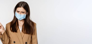 Coronavirus ve insanlar konsepti. Ofis kıyafetleri ve tıbbi yüz maskesi takmış üzgün, sol üst köşeyi gösteren, beyaz arka planı olan üzgün ve endişeli bir kadın..