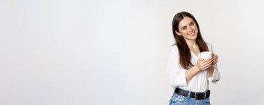 Corporate woman standing with coffee tea mug and smiling, drinking from cup, standing happy against white background.