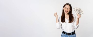 Joyful woman dancing with money, smiling pleased, winning prize, standing over white background.