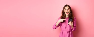 Genç bir kadın telefonunu işaret ediyor ve gülümsüyor. Akıllı telefon uygulamasından bahsediyor. İnternette ilginç bir şey gösteriyor..