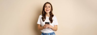 Happy modern woman smiling, holding smartphone and laughing, concept of cellular technology and mobile phone.